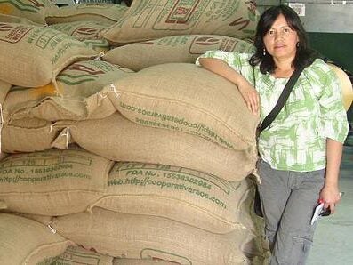 Mayra Orellana-Powell standing next to piles of big shipping coffee bags.