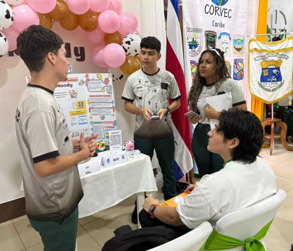 Josimar Madrigal and his teammates stand behind their "Moody" app display table at a student innovation showcase in Costa Rica.